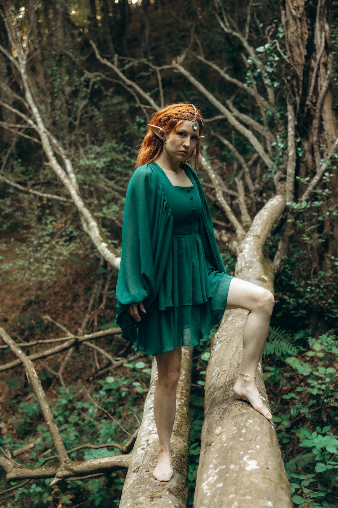 A woman in a green dress is standing on a tree branch